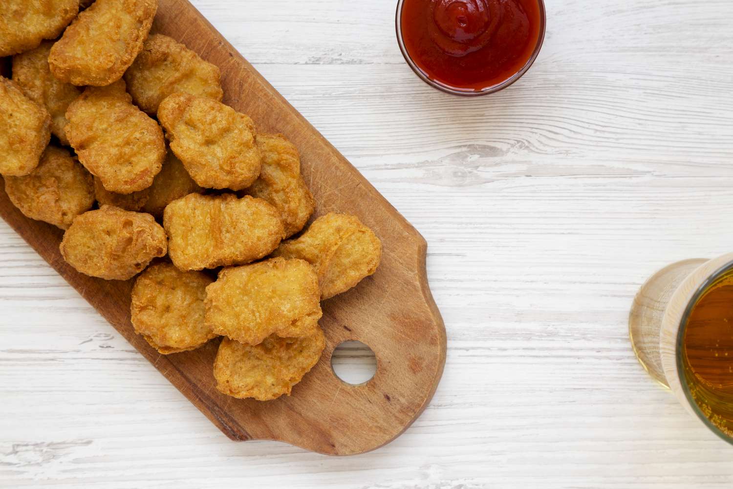 Chicken nuggets with ketchup and glass of cold beer on a white wooden table, overhead view. Flat lay, from above, top view. Close-up.