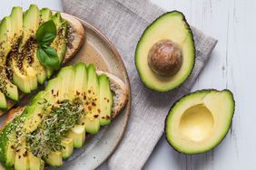 Avocado toast and a halved avocado on wooden table