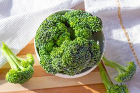 Top view of bright green organic raw broccoli branches in the white bowl on the table in the kitchen close up.