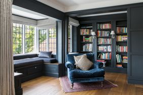 Dark blue home library with velvet chair and window area