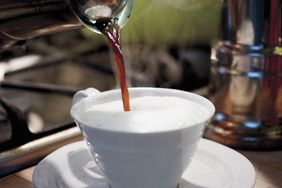 adding coffee to steamed milk in a cup