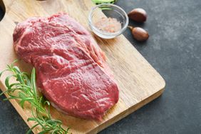 Steak on cutting board next to rosemary and salt 