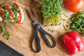 Kitchen shears on cutting board with greens and vegetables