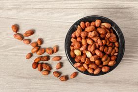 Top view of peanuts in black porcelain bowl and beside it on grey wooden background