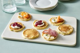 Silver dollar pancakes with fruit, meat, cheese on white plate