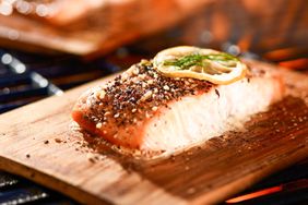 salmon fillets cooking on cedar planks on grill