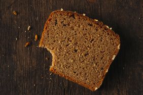 Slice of bread missing bite and crumbs on wood surface