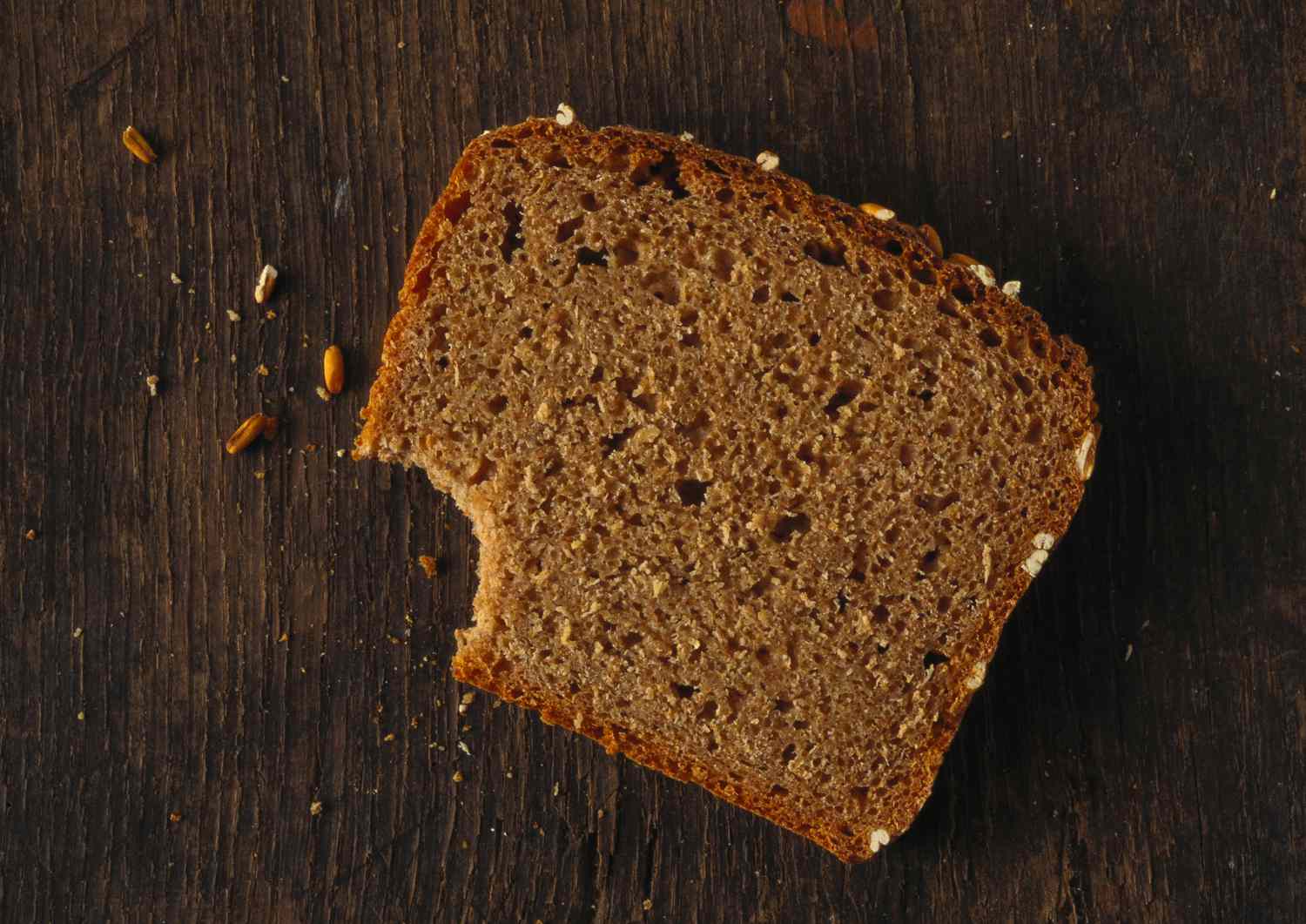 Slice of bread missing bite and crumbs on wood surface