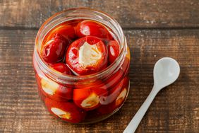 Stuffed cherry peppers with ricotta cheese filling in glass jar on wooden background